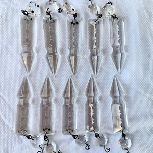 Peut inclure: Cristaux de lustre en verre transparent de différentes formes, dont des pendentifs pointus et des gouttelettes à facettes. Les cristaux sont reliés par une quincaillerie en métal noir et de petites perles transparentes. L'arrangement est sur fond blanc.