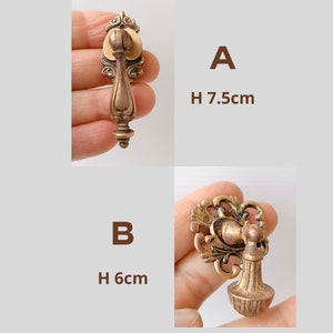 Pode incluir: Duas puxadores de gaveta antigos em bronze. O puxador A tem 7,5 cm de altura, com uma placa traseira decorativa e uma pega em forma de gota. O puxador B tem 6 cm de altura, com uma placa traseira ornamentada e uma pega em forma de sino.