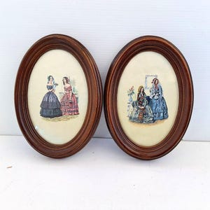 Può includere: Due stampe ovali incorniciate con illustrazioni di donne in abiti d'epoca. Le cornici sono in legno marrone scuro. Le stampe raffigurano donne in abiti colorati, con sfondi e ambientazioni dettagliate.