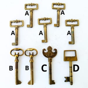Peut inclure: Collection de clés anciennes en laiton avec différents modèles de poignées, étiquetées A, B, C et D. Les poignées présentent des détails ornementaux, notamment des motifs floraux et enroulés. Les clés présentent des signes d'usure variables.