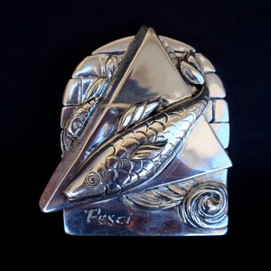 May include: Silver-toned metal sculpture of the Pisces zodiac sign. The sculpture features two fish swimming in a triangular frame with the word "Pisces" inscribed below.