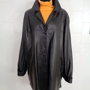 May include: A black leather jacket with a button closure and long sleeves. The jacket is on a white tiled background.