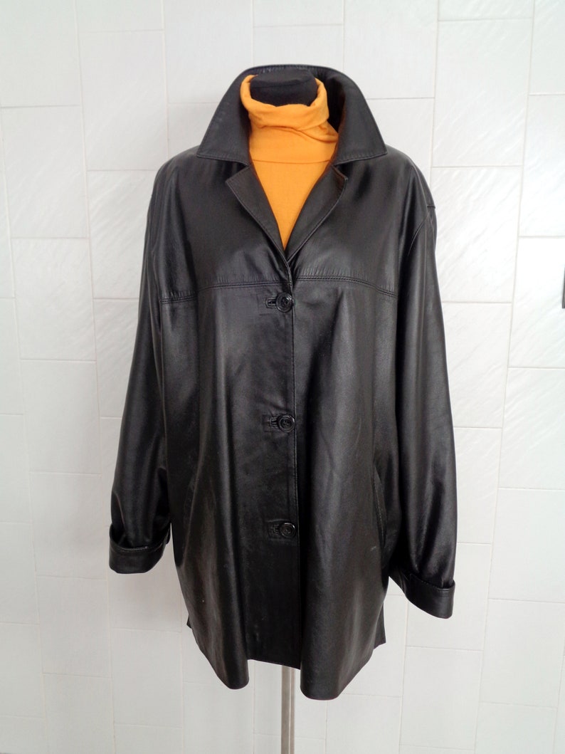 May include: A black leather jacket with a button closure and long sleeves. The jacket is on a white tiled background.