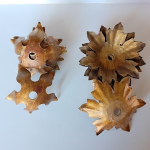 Op de afbeelding: Twee sets decoratieve, goudkleurige metalen objecten in de vorm van bloemen. Elke bloem heeft meerdere bloemblaadjes en een gat in het midden. Het metaal heeft een licht verweerde afwerking, waardoor het een vintage uitstraling heeft.