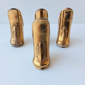 May include: Four vintage gold-coloured decorative objects. The objects have a curved, elongated shape with a textured surface. The objects are arranged on a white surface. The objects appear to be made of metal or a similar material.