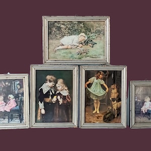 Può includere: Una collezione di cinque stampe vintage incorniciate. Le stampe raffigurano bambini in varie scene, tra cui giocare con i cani, condividere una leccornia e riposare all'aperto. Le cornici argentate e le opere d'arte hanno un'atmosfera classica e nostalgica.