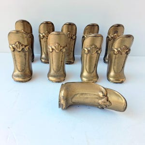 Può includere: Una collezione di piedini per mobili antichi in ottone, ciascuno con un motivo floreale decorativo. I piedini hanno una calda patina invecchiata, che suggerisce che siano vintage o di ispirazione vintage. I piedini sono disposti su una superficie bianca.