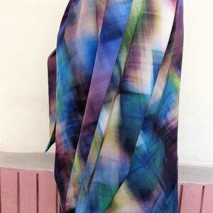 May include: A colorful, abstract-patterned blouse in shades of blue, green, purple, and yellow. The fabric drapes softly, suggesting a lightweight material. The blouse is worn over a black garment.