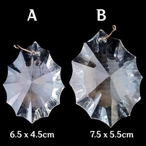 May include: Two clear, faceted crystal pendants with a starburst design. The smaller pendant measures 6.5 x 4.5cm, and the larger one is 7.5 x 5.5cm. Each has a wire loop for hanging. The background is black.