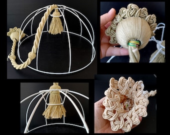 Puede incluir: Una pantalla de lámpara de alambre blanco con detalles de cuerda y borlas beige. El diseño incluye un asa decorativa de cuerda y una borla central. La pantalla de la lámpara está adornada con intrincados detalles de nudos, mostrando una estética artesanal.