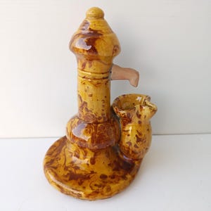 May include: A ceramic well pump figurine with a brown and yellow marbled glaze. The pump has a spout and a bucket.