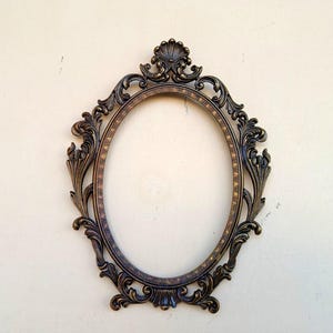 Puede incluir: Un marco de fotos ovalado adornado con un acabado dorado y detalles intrincados. El marco está hecho de metal y tiene un diseño clásico.