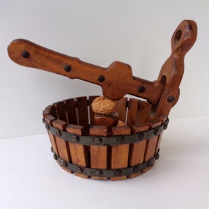 Könnte beinhalten: Ein Nussknacker aus Holz mit einem Griff und einem Korb zum Aufbewahren der Nüsse. Der Nussknacker ist aus braunem Holz gefertigt und hat Metallverzierungen.