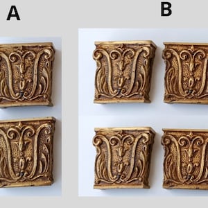 Könnte beinhalten: Zwei Sätze antiker, goldfarbener dekorativer Architekturelemente. Jedes Element ist rechteckig mit aufwendigen, symmetrischen Blumen- und Rankenmustern. Die Elemente haben ein verwittertes Aussehen, das auf Alter und Nutzung hindeutet. Der Hintergrund ist hellgrau.