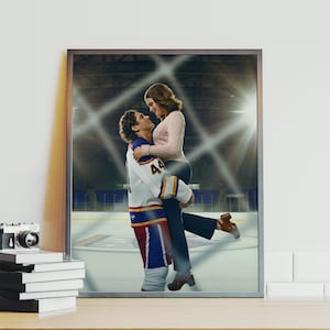 May include: Framed print featuring a couple embracing on an ice hockey rink. The man wears a hockey jersey with the number 44. The woman is wearing a pink sweater and dark pants. The background shows the arena.