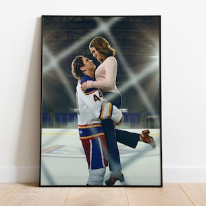 May include: Framed print featuring a man in a hockey uniform lifting a woman. The man's jersey is white, blue, and red with the number 44. The woman wears a pink sweater and dark pants. The background shows an ice rink.