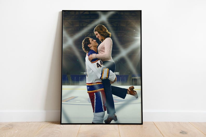 May include: Framed print featuring a man in a hockey uniform lifting a woman. The man's jersey is white, blue, and red with the number 44. The woman wears a pink sweater and dark pants. The background shows an ice rink.