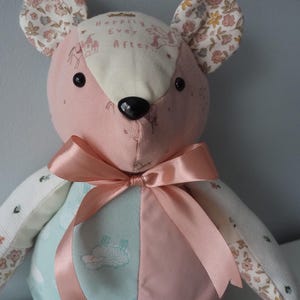 May include: A stuffed animal mouse made of multi-colored fabric patches. The head features pink fabric with a cream-colored forehead patch printed with the text "Happily Ever After" and a castle graphic. It has a satin ribbon bow and floral ears.