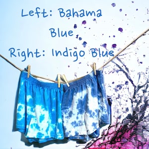 May include: Two pairs of tie-dye shorts hanging on a clothesline. The shorts on the left are a lighter blue color, labeled "Bahama Blue". The shorts on the right are a darker blue color, labeled "Indigo Blue".