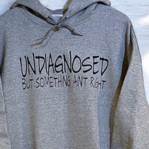 May include: A gray hooded sweatshirt with the text "Undiagnosed but something ain't right" printed in black.