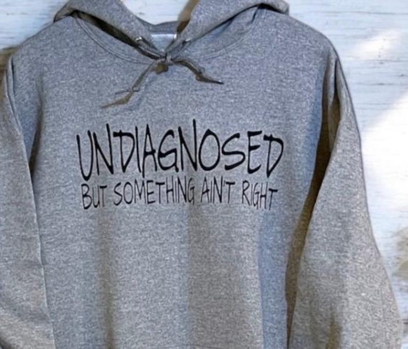 May include: A gray hooded sweatshirt with the text "Undiagnosed but something ain't right" printed in black.
