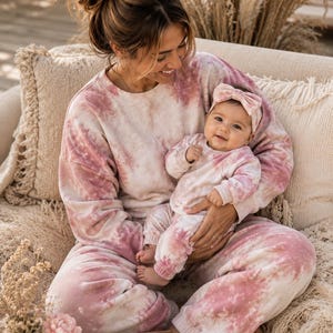Könnte beinhalten: Ein zweiteiliges Set aus rosa und weißem Tie-Dye. Eine Person hält ein Baby in einem passenden Outfit und Stirnband. Die Kleidung ist weich und bequem, ideal zum Entspannen oder für Freizeitkleidung.