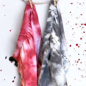 May include: Two tie-dye fabric panels hanging on a clothesline with wooden clothespins. The panel on the left is pink and white, and the panel on the right is gray and white.