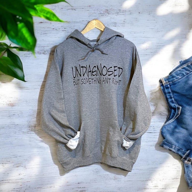 May include: Gray hooded sweatshirt with the text "UNDIAGNOSED BUT SOMETHING AINT RIGHT" printed in black.