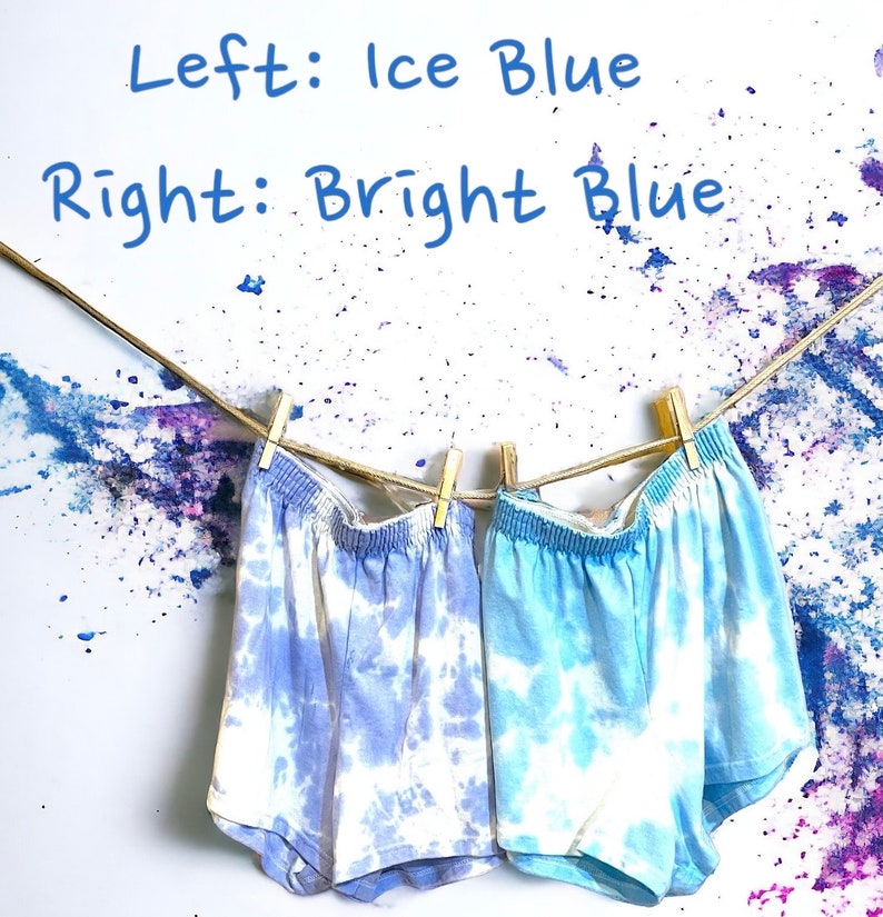 May include: Two pairs of tie-dye shorts hanging on a clothesline. The shorts on the left are a lighter ice blue color, while the shorts on the right are a brighter blue. The text "Left: Ice Blue" and "Right: Bright Blue" is written above the shorts.