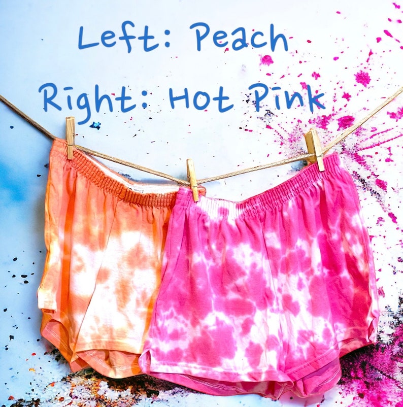 May include: Two pairs of tie-dye shorts hanging on a clothesline. The shorts on the left are peach colored with white tie-dye. The shorts on the right are hot pink with white tie-dye. Left: Peach. Right: Hot Pink.