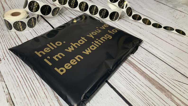 May include: Black poly mailer with gold text reading "hello. I'm what you've been waiting for." Rolls of stickers with gold and black design are in the background. The stickers say "Planet Taste".