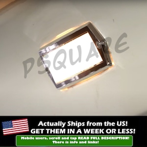 May include: A chrome-plated rectangular car light with a white lens. The light is illuminated and casting a warm glow.