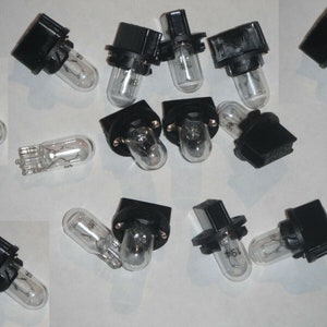 Puede incluir: Un grupo de 13 bombillas de luz negras y transparentes con base de bayoneta. Las bombillas están dispuestas en un patrón aleatorio sobre una superficie blanca.