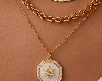 May include: A layered gold necklace set consisting of a flat herringbone chain, a medium-weight oval link chain, and a delicate cable chain featuring an octagonal pendant with a white inlay, a central starburst design, and small clear stones.