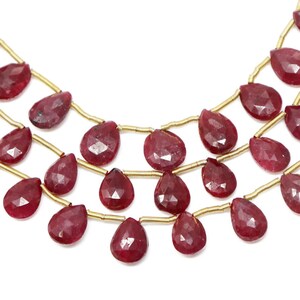 以下が含まれることがあります： 金色のワイヤーに赤いルビーの宝石ビーズが通されたネックレス。ビーズはファセットカットされており、涙の形をしています。