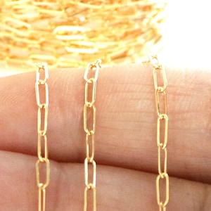 Puede incluir: Tres hebras de cadena de oro con un diseño de eslabón rectangular. La cadena se muestra en una mano.