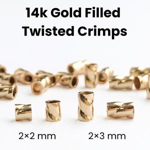 May include: Gold-filled twisted crimps in various sizes. The image shows several gold-colored crimps, some scattered and others arranged in a row. The text reads "14K Gold Filled Twisted Crimps" and indicates sizes of 2x2 mm and 2x3 mm.