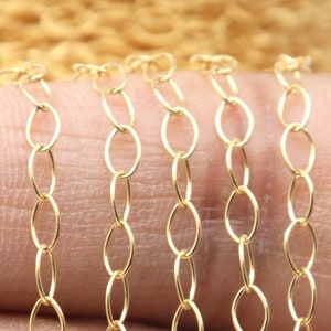 May include: A close-up of a gold chain with oval links. The chain is lying on a person's finger.