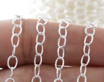 May include: Silver chain with a textured oval link design. The chain is shown in a hand, with multiple strands of the chain.