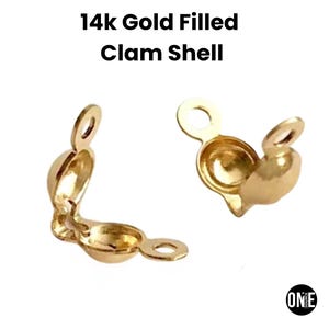 Puede incluir: Dos cierres de concha de almeja rellenos de oro de 14k. Los cierres están abiertos, revelando el interior. Cada cierre tiene un pequeño lazo en la parte superior y una forma de concha redondeada. El texto "14k Gold Filled Clam Shell" está en la parte superior.
