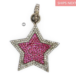 Puede incluir: Un colgante de estrella de plata con un centro de rubí rosa y un borde de diamantes.
