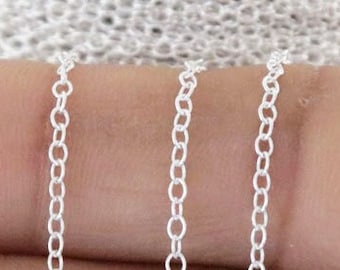 May include: A close-up of a silver chain, shown in multiple strands, with a delicate, round link design.