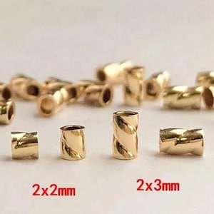 May include: Gold-colored metal beads in two sizes, 2x2mm and 2x3mm. The beads have a twisted design and are arranged in a row on a white surface.
