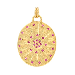 May include: A gold pendant with a circular design featuring a central cluster of pink gemstones surrounded by smaller pink gemstones.