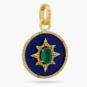 K&ouml;nnte beinhalten: Ein goldener Anh&auml;nger mit einem blauen Emaille-Oval-Anh&auml;nger, der einen gr&uuml;nen Edelstein zeigt, der von einem Sternburst-Design mit klaren Steinen umgeben ist.