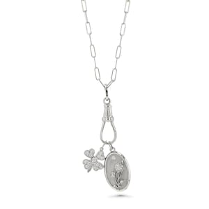 May include: A silver-toned necklace with a paperclip chain design. The necklace features a clasp with two charms: a four-leaf clover and an oval pendant with a floral design, both adorned with small, sparkling stones.
