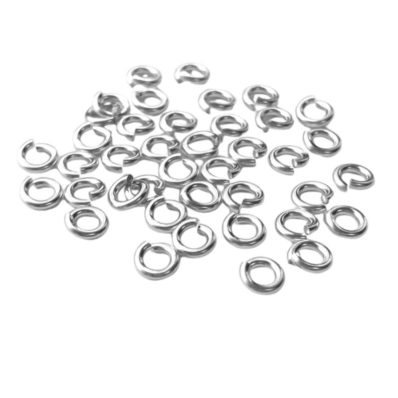 May include: A collection of small, silver-colored split rings, scattered against a white background. These open jump rings are used in jewelry making and other crafts. The rings are made of a shiny, metallic material.