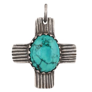 May include: A silver pendant in the shape of a cross with a turquoise stone in the center. The cross has a decorative design with lines.