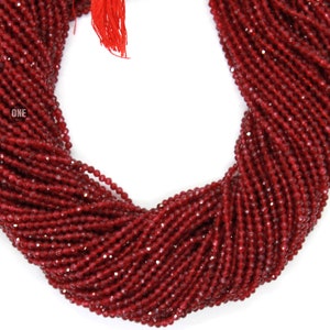 May include: Strands of small, faceted, deep red beads. The beads are tightly strung together, forming a thick, flowing shape. A red tassel hangs from the top. The word "ONE" is visible on the left side.