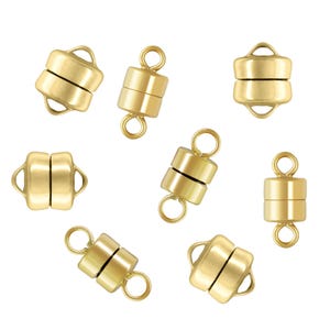 May include: Several gold-colored magnetic clasps for jewelry making are scattered on a white background. Each clasp is cylindrical with a loop on each end and a magnetic closure in the middle. The clasps are shown both connected and separated.